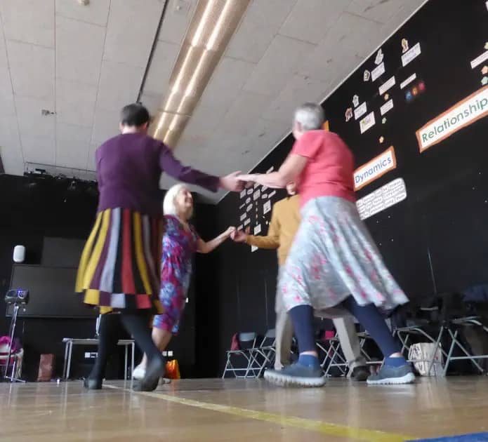 4 dancers holding hands moving to the left in a circle